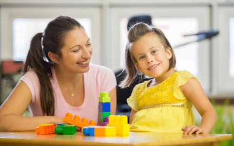 Young Woman Playing With Child At Table With Building Blocks