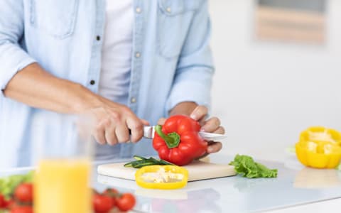 Man Slicing Peppers In Chopping Board In Kitchen