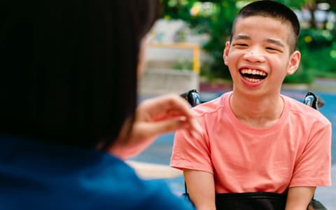 Child In Wheelchair Smiling At Adult