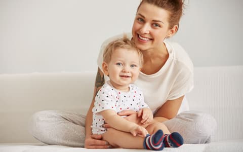 Mother Sitting With Child On Bed Smiling