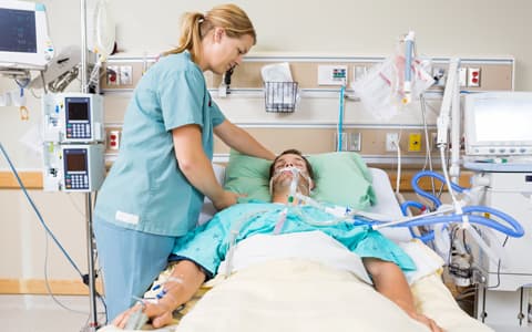 Patient In Bed On Oxygen With Nurse Attending To Them